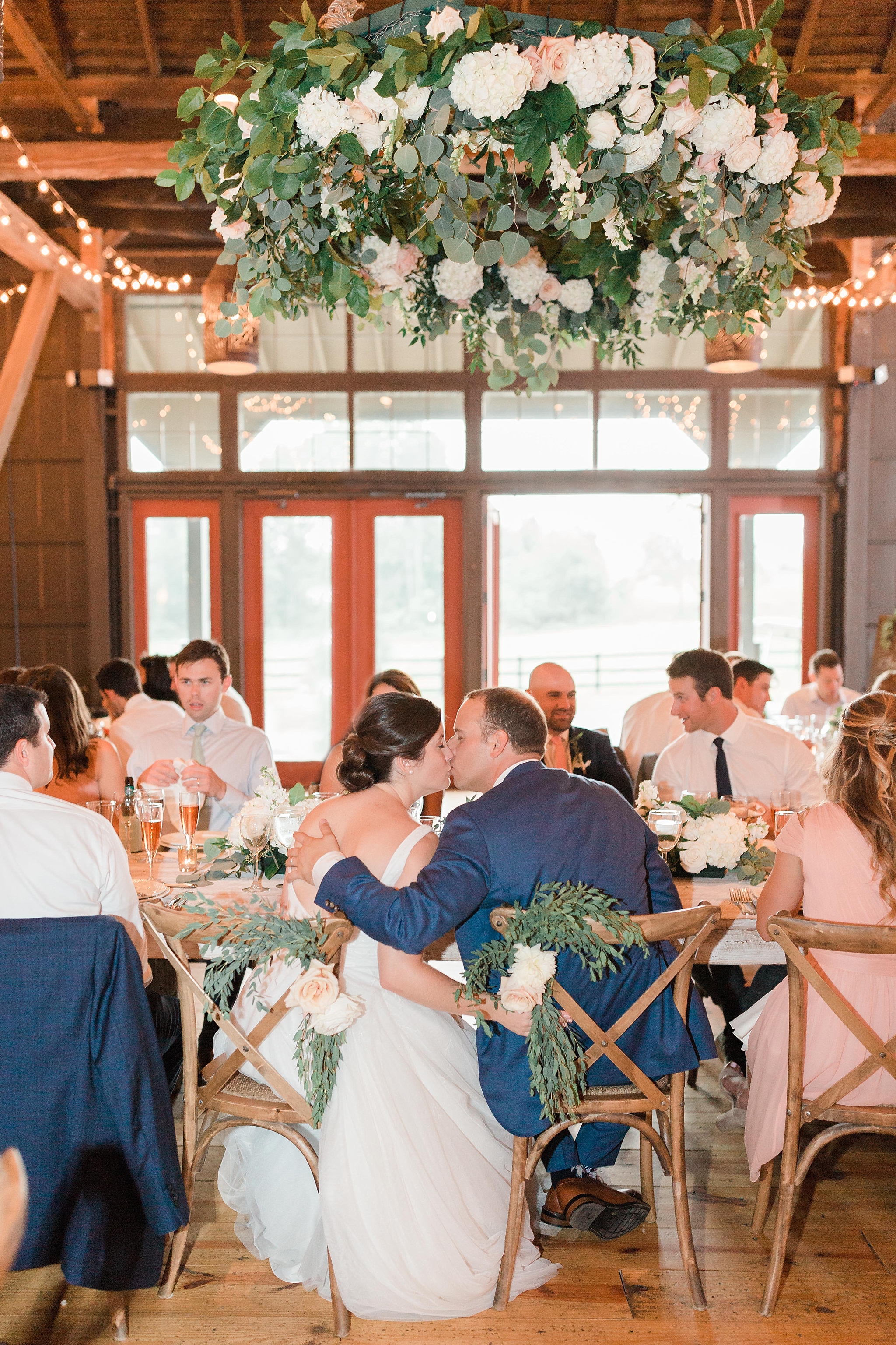 A romantic and chic wedding at Riverside on the Potomac in Leesburg, VA features a neutral palette of creams and greens with a stunning floral chandelier inside the barn!